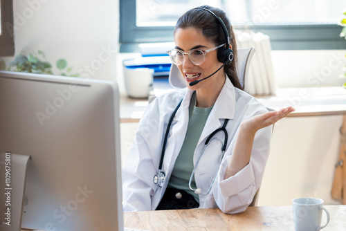 Female doctor explaining medical treatment to patient through a video call with laptop and earphones in the consultation