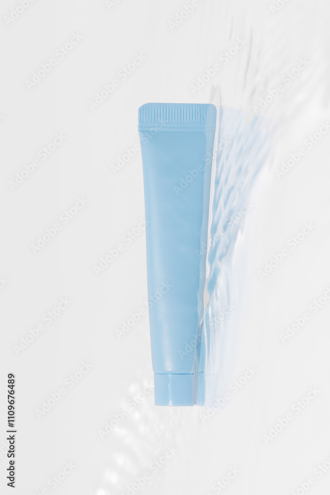 Vertical image of blue mockup tube of cream in water with reflection on white background. Concept of beauty products, facial skin care Vertical image of blue mockup tube of cream in water with reflection on white background. Concept of beauty products, facial skin care