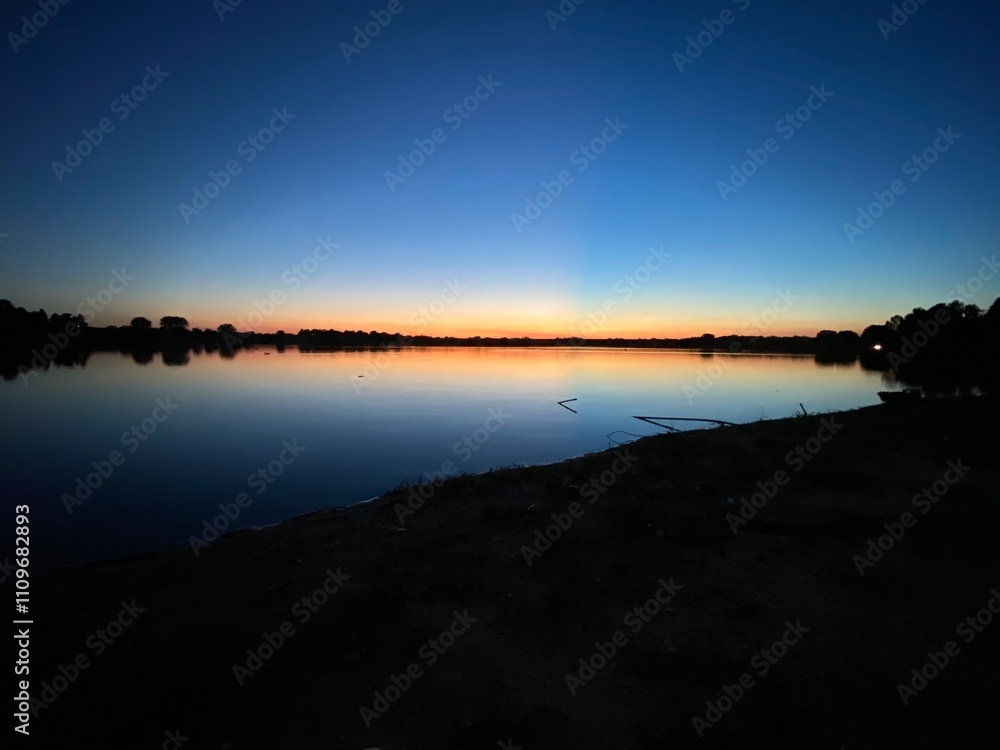 Beautiful summer sunset over a lake at night from the shore, reflections over the water, at Holmes Park in Lincoln, Nebraska, United States Beautiful summer sunset over a lake at night from the shore, reflections over the water, at Holmes Park in Lincoln, Nebraska, United States