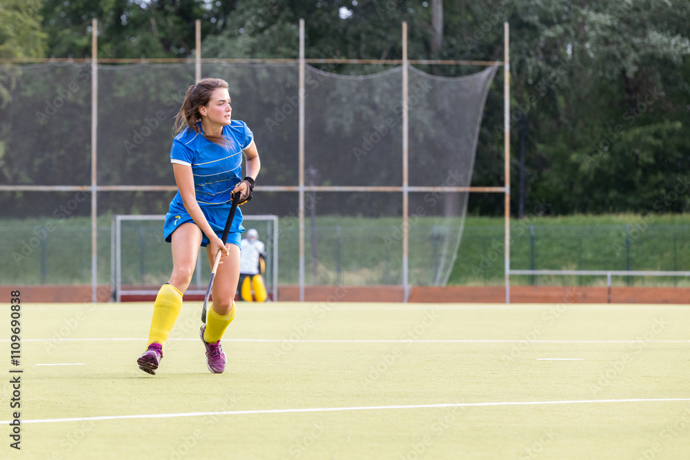 Female athlete in blue uniform running along the pitch during field hockey game Female athlete in blue uniform running along the pitch during field hockey game