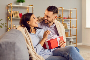 Young affectionate couple in love, pair wrapped with warm blanket enjoy happy romantic holiday, gift present box giving, feeling close, Saint Valentine's Day celebration at home, festive studio