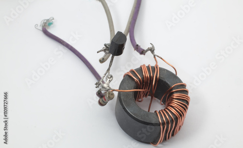 Photos A ferrite core toroid ring with copper windings connected to a resistor and a transistor on a white background