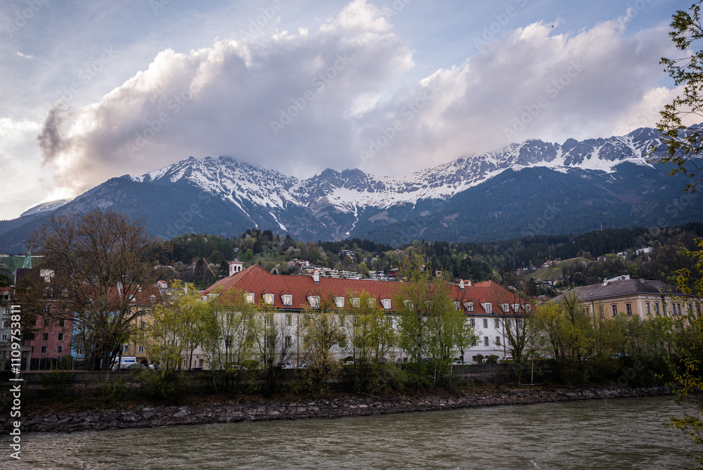 Fototapeta premium Innsbruck, Austria, on Easter Day, with scenic views of the Inn River and historic buildings against a backdrop of the Alps and vibrant skies