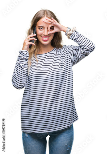 Beautiful young blonde woman talking on smarpthone over isolated background with happy face smiling doing ok sign with hand on eye looking through fingers