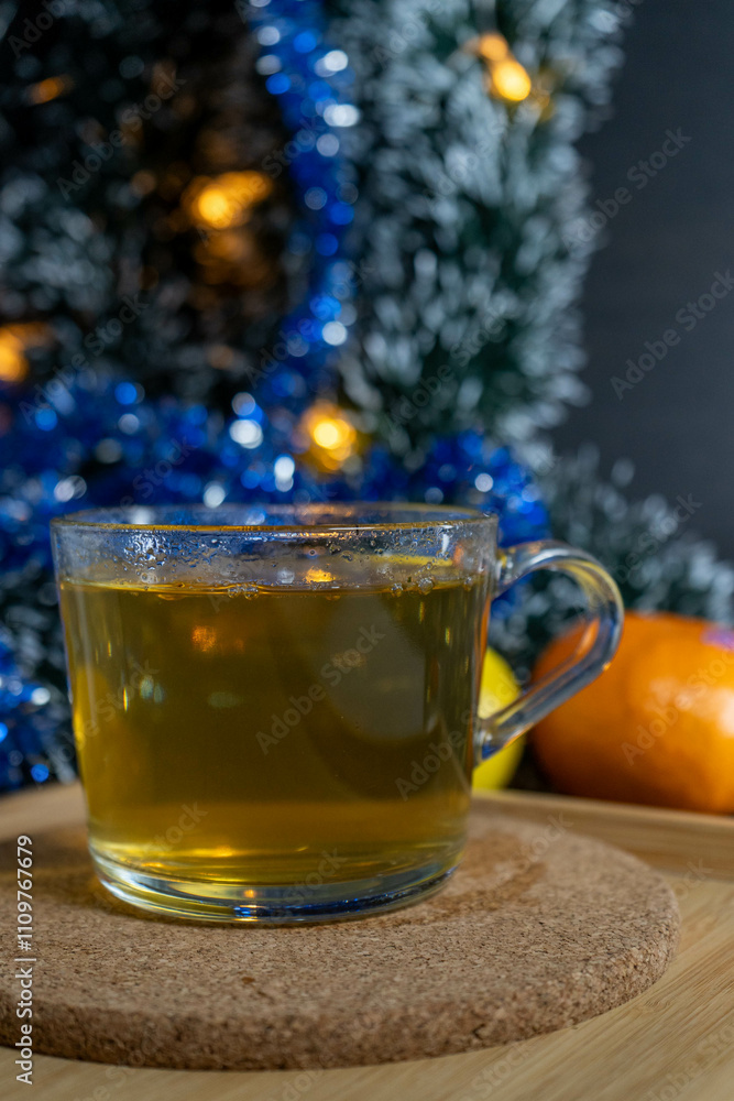 A transparent cup of green tea surrounded by citrus fruits and a Christmas tree, creating a festive atmosphere. A transparent cup of green tea surrounded by citrus fruits and a Christmas tree, creating a festive atmosphere.