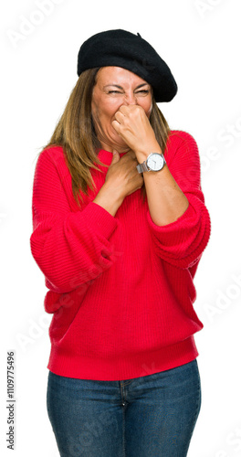 Middle age adult woman wearing fashion beret over isolated background smelling something stinky and disgusting, intolerable smell, holding breath with fingers on nose. Bad smells concept. photo