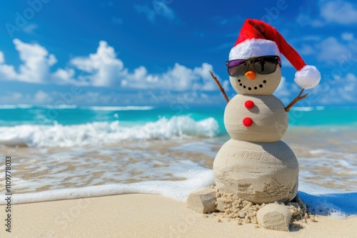 A cheerful sand snowman wearing sunglasses and a Santa hat stands on the beach, with clear blue waves and sky in the background