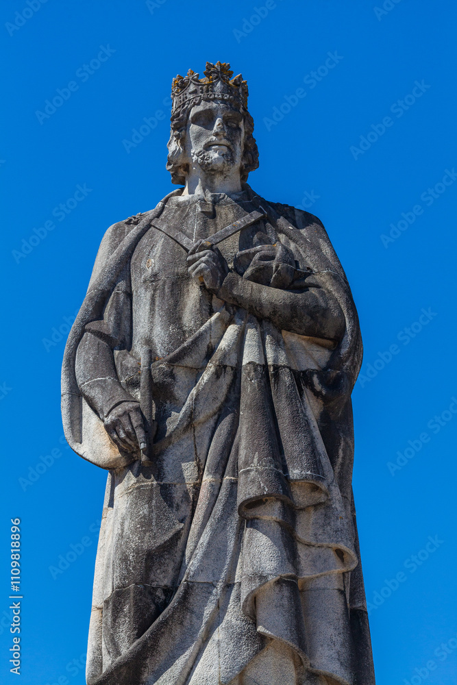 Obraz premium A statue of King Dinis I of Portugal stands tall in Coimbra, Portugal, with the city's clock tower in the background