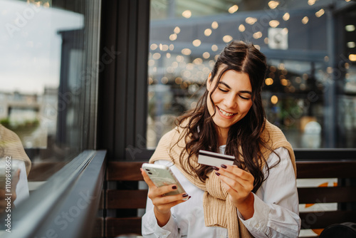 Young caucasian woman using credit card in cafe to pay from her phone	
