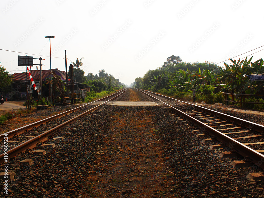 Naklejka premium View of the intersection between two railway tracks and a road on a sunny day.