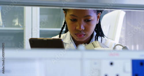 Scientist looking through microscope while using digital tablet in laboratory