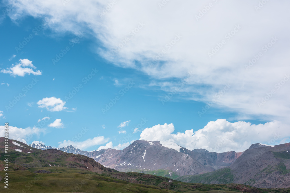 Dramatic alpine view from green hills to large rocky mountain range with glacier under clouds in blue sky. Scenic landscape with big snow mountain top. Changeable cloudy weather in high mountains. Dramatic alpine view from green hills to large rocky mountain range with glacier under clouds in blue sky. Scenic landscape with big snow mountain top. Changeable cloudy weather in high mountains.