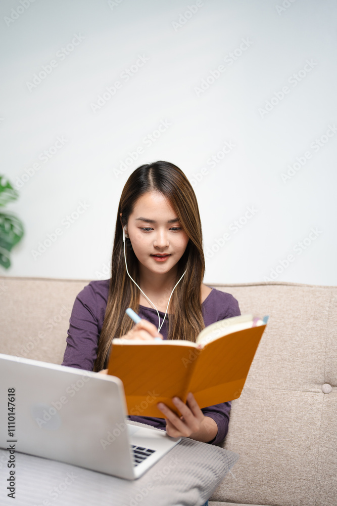 young asian female in earphones writing and taking note look at laptop screen study online on gadget. Happy female in earphones work distant on computer. Education concept. young asian female in earphones writing and taking note look at laptop screen study online on gadget. Happy female in earphones work distant on computer. Education concept.