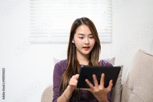 Modern lady having relax at home sitting on couch and using e reader tablet to read an online ebook. Woman using technology indoor leisure activity alone enjoying relaxation on couch. Indoor life