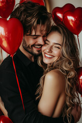 Happy young couple holding red balloons shaped heart standing on studio room. Valentine's day celebration