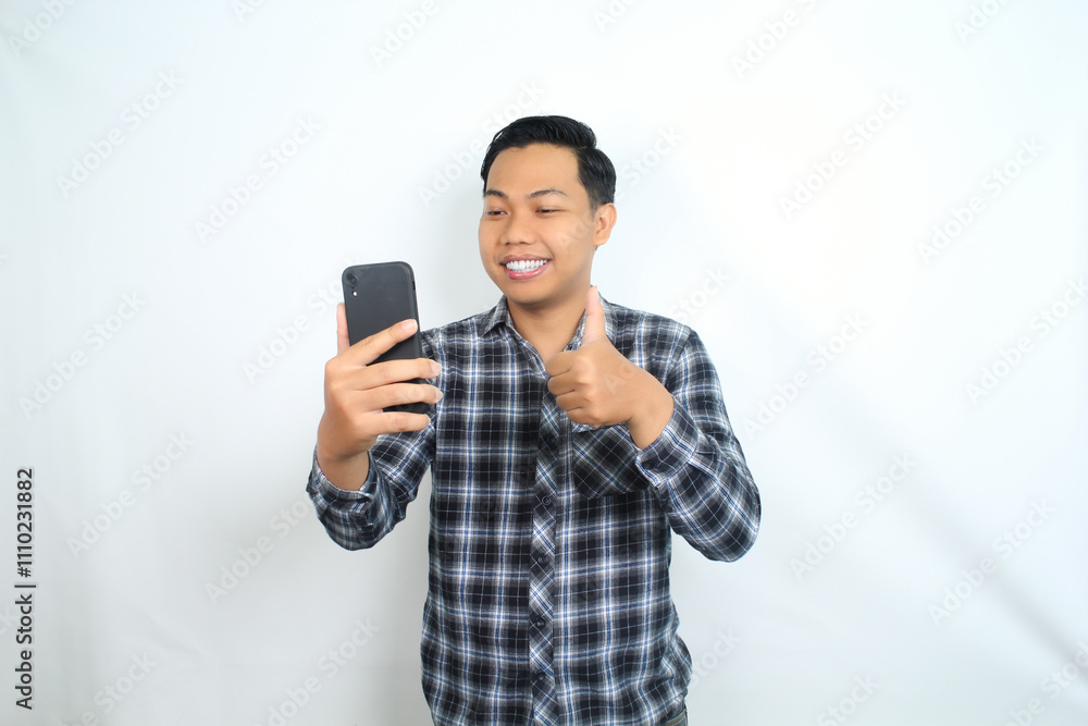 smiling asian man showing thumb up with holding mobile phone wear casual shirt isolated on white