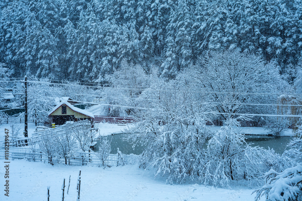 heavy snow in winter landscape with house, lake and forest.