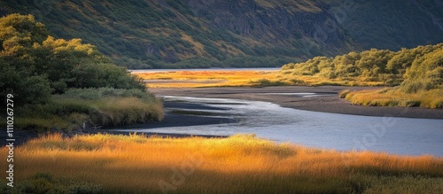 Lush green and vibrant yellow fields meet a serene silver river in a picturesque valley landscape evoking a dreamlike atmosphere. photo