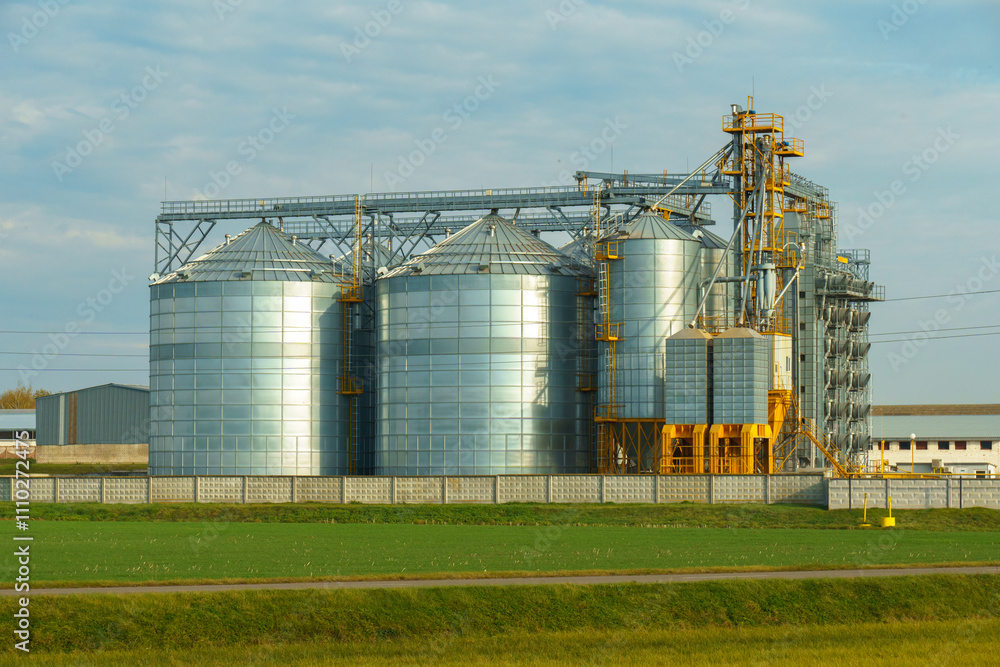 Silver silos in the field. A modern grain storage, processing and drying plant against the background of a sunset sky. Grain delivery and transportation. Silver silos in the field. A modern grain storage, processing and drying plant against the background of a sunset sky. Grain delivery and transportation.