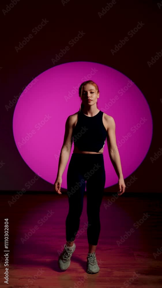 A sporty woman in a black suit and red hair posing on a pink background. Portrait of a female athlete. The concept of sports and a healthy lifestyle. Vertical video 4k A sporty woman in a black suit and red hair posing on a pink background. Portrait of a female athlete. The concept of sports and a healthy lifestyle. Vertical video 4k