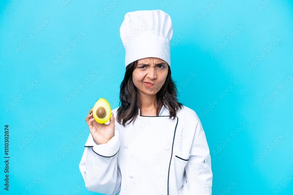 Young hispanic chef woman holding avocado isolated on blue background having doubts Young hispanic chef woman holding avocado isolated on blue background having doubts