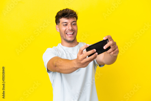 Young caucasian handsome man isolated on yellow background playing with the mobile phone