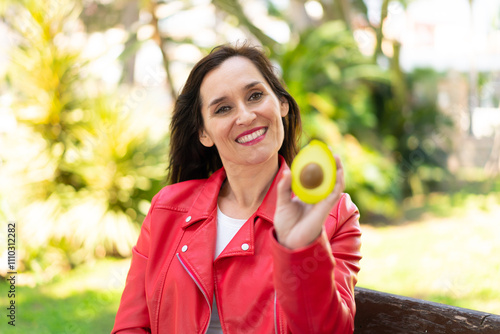 Middle aged woman holding an avocado at outdoors with happy expression