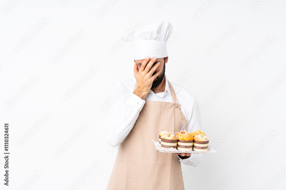 Young man holding muffin cake over isolated white background with tired and sick expression Young man holding muffin cake over isolated white background with tired and sick expression