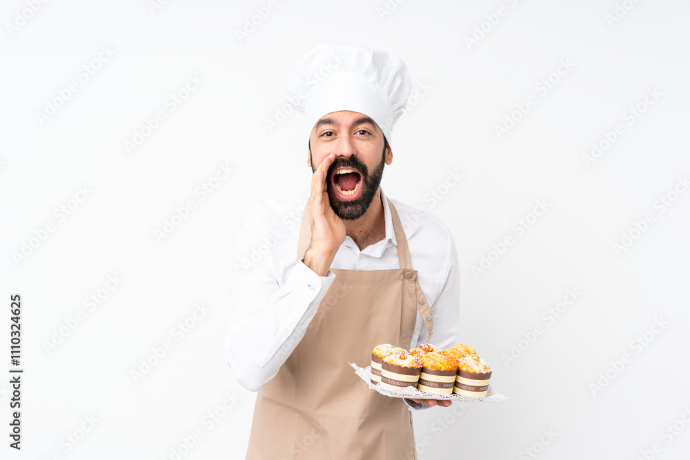 Young man holding muffin cake over isolated white background shouting and announcing something Young man holding muffin cake over isolated white background shouting and announcing something
