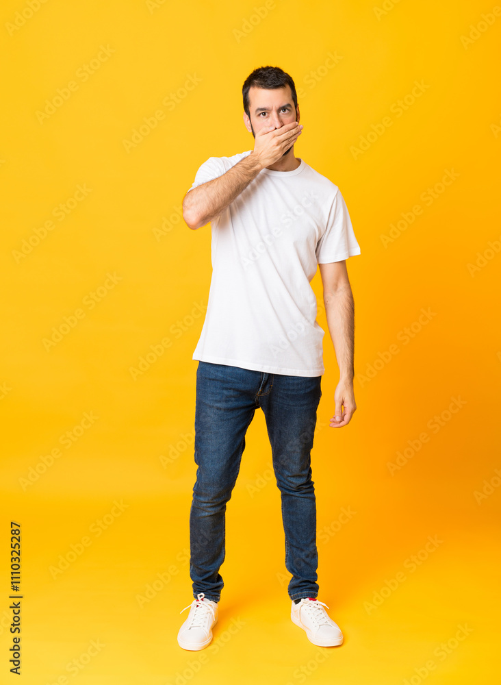 Full-length shot of man with beard over isolated yellow background covering mouth with hands