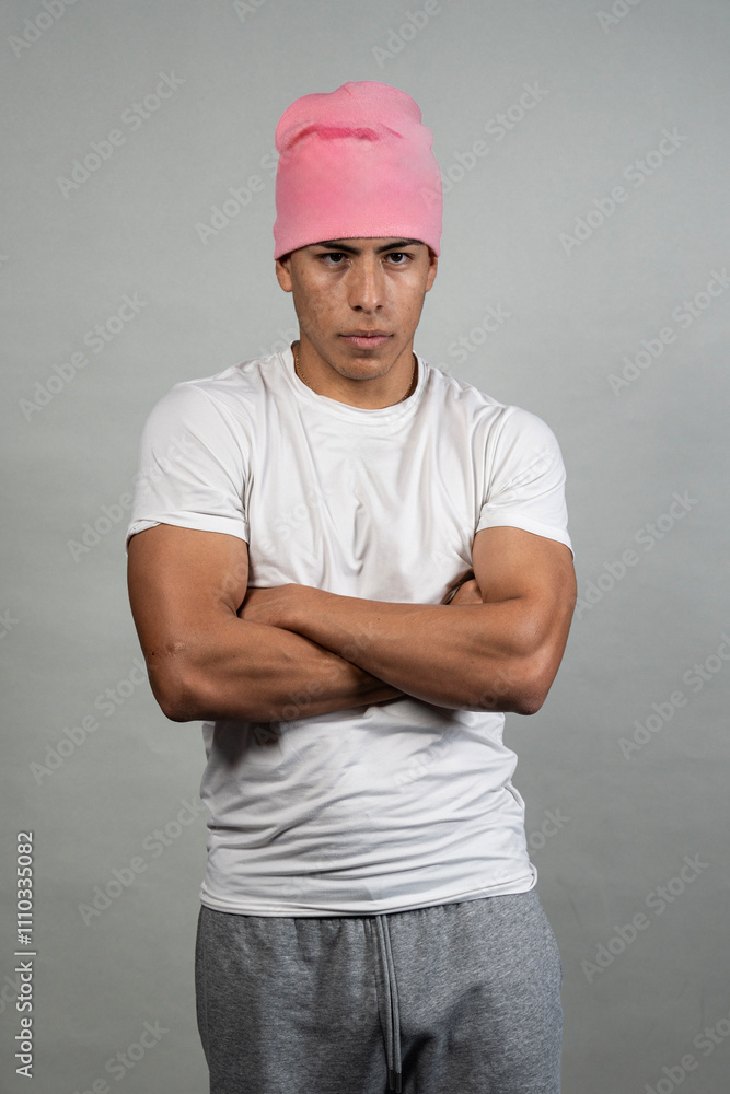 Serious latino man wearing pink beanie with crossed arms on gray background Serious latino man wearing pink beanie with crossed arms on gray background