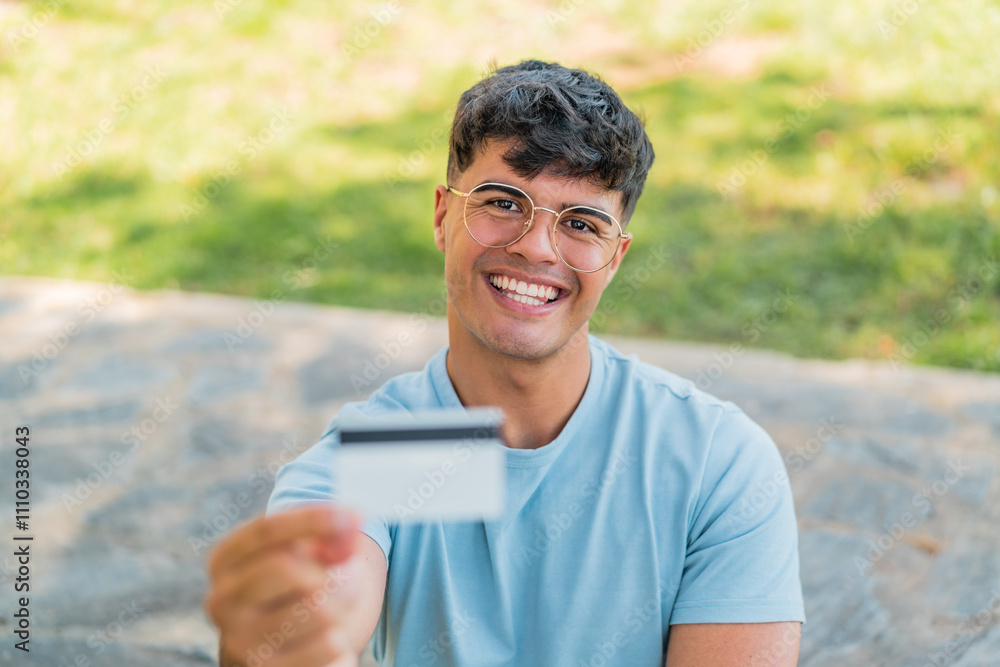 Young hispanic man holding a credit card at outdoors with happy expression Young hispanic man holding a credit card at outdoors with happy expression