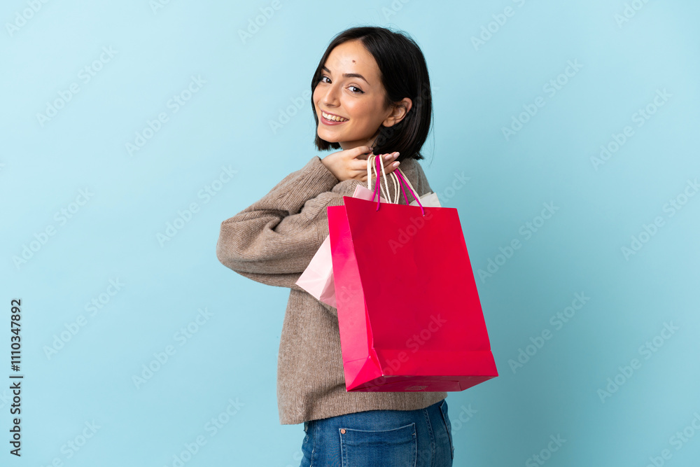 Young caucasian woman isolated on blue background holding shopping bags and smiling Young caucasian woman isolated on blue background holding shopping bags and smiling