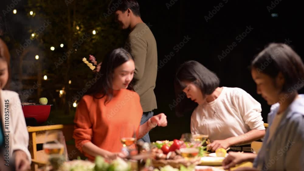 A group of people are sitting around a table with food and drinks. The man in the brown shirt is serving food to the woman in the orange shirt. Scene is warm and inviting A group of people are sitting around a table with food and drinks. The man in the brown shirt is serving food to the woman in the orange shirt. Scene is warm and inviting