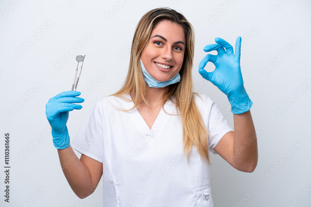 Dentist woman holding tools isolated on white background showing ok sign with fingers Dentist woman holding tools isolated on white background showing ok sign with fingers