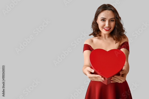 Beautiful young woman with gift box on grey background