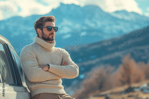  A man in a casual sweater and khaki pants, leaning against a car with a scenic mountain view in the background with copy space. Cool light. Road trip background. photo