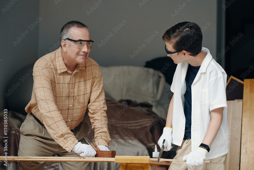 Grandfather teaching his son to saw the wood in the workshop Grandfather teaching his son to saw the wood in the workshop