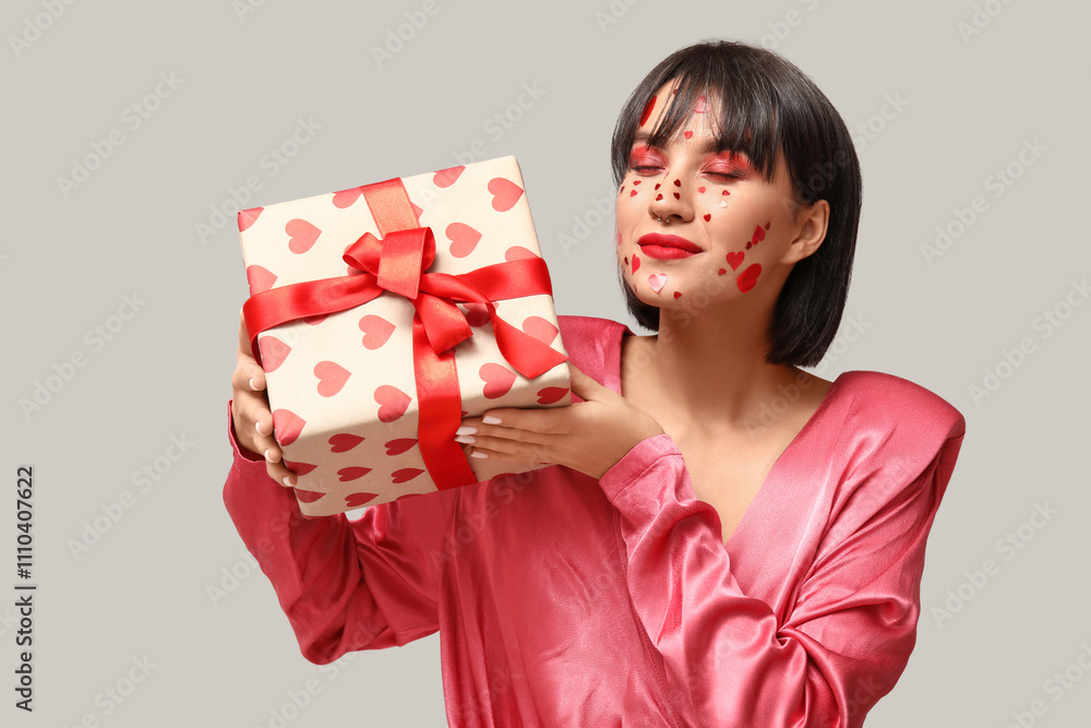 Beautiful young woman with creative makeup and gift for Valentines Day on grey background Beautiful young woman with creative makeup and gift for Valentines Day on grey background