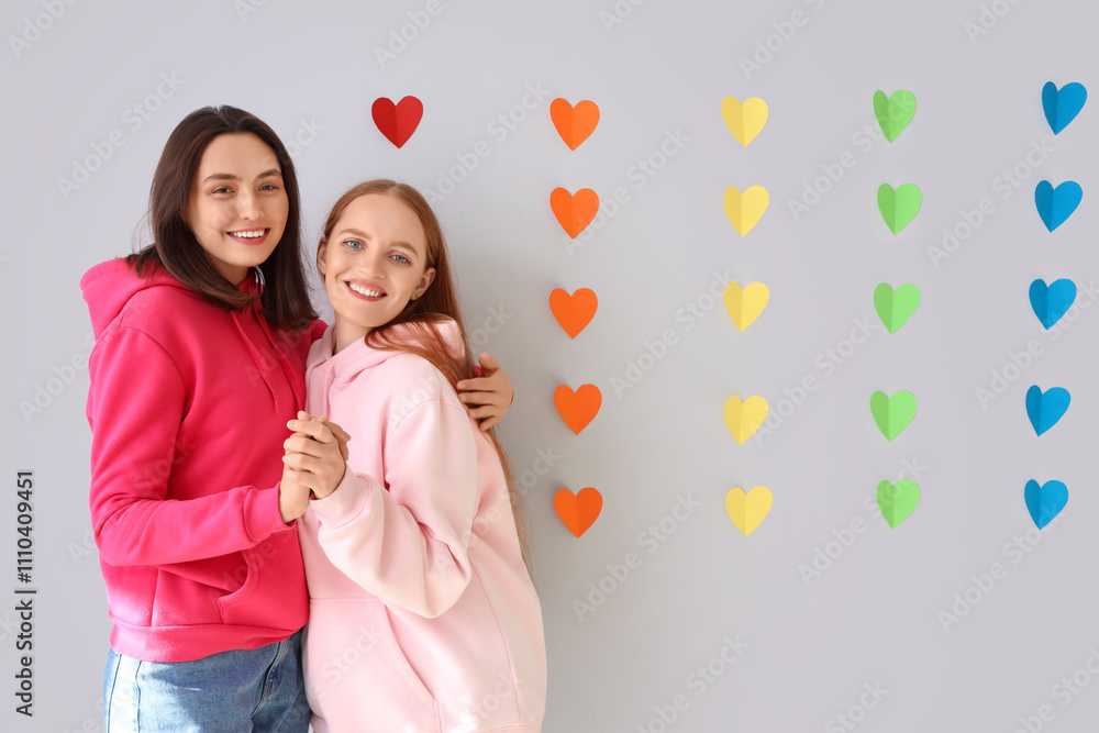 Young lesbian couple hugging and rainbow hearts on light background. Valentine's Day celebration Young lesbian couple hugging and rainbow hearts on light background. Valentine's Day celebration