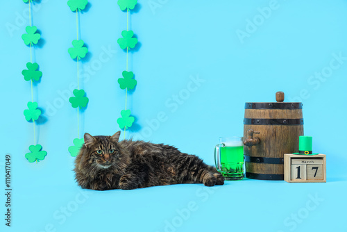 Cute cat with barrel of beer, calendar and decor for St. Patrick's Day celebration on blue background photo