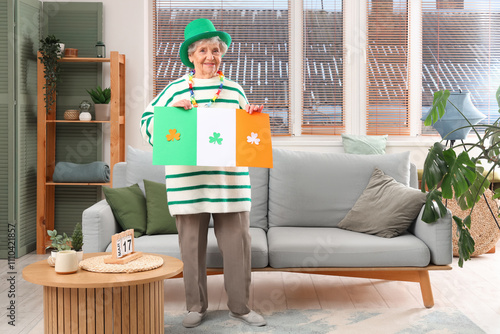 Senior woman in leprechaun hat with paper Irish flag for St. Patrick's Day celebration at home photo