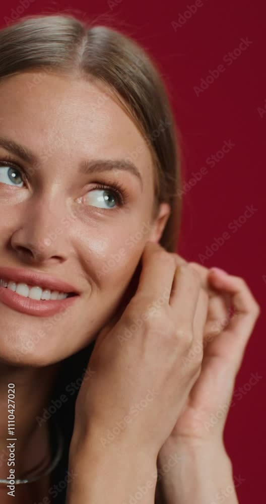 A woman in formal clothes puts on earrings while standing on a studio background. She smiles at the camera A woman in formal clothes puts on earrings while standing on a studio background. She smiles at the camera