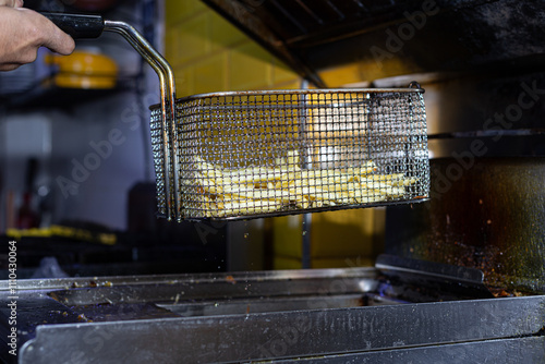 Obraz na płótnie Hot, golden fries are pulled from an industrial fryer, their crispy texture glistening with oil. A satisfying moment that every fry enthusiast can appreciate. w salonie