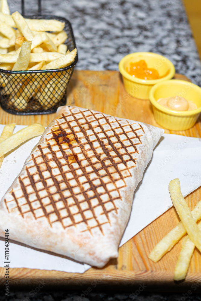 A satisfying fast-food combo of grilled wrap, golden fries, and creamy dips on a wooden presentation.