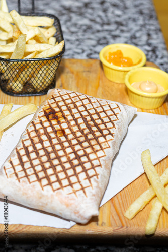 Obraz na płótnie A satisfying fast-food combo of grilled wrap, golden fries, and creamy dips on a wooden presentation. w salonie