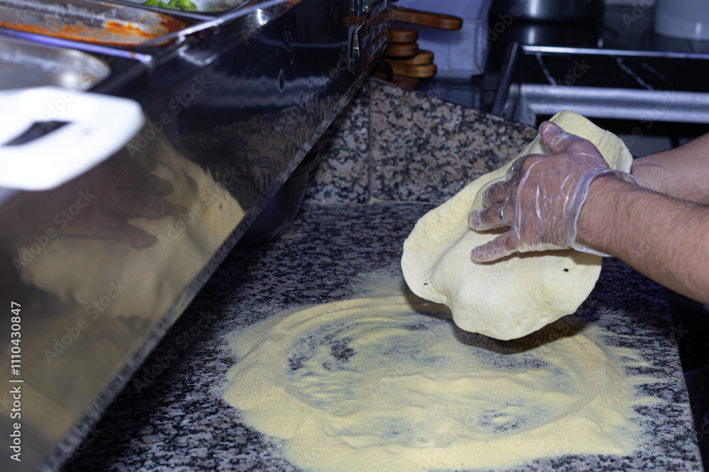 A handmade pizza base takes form under the skilled hands of a pizza maker, showcasing attention to detail and quality.