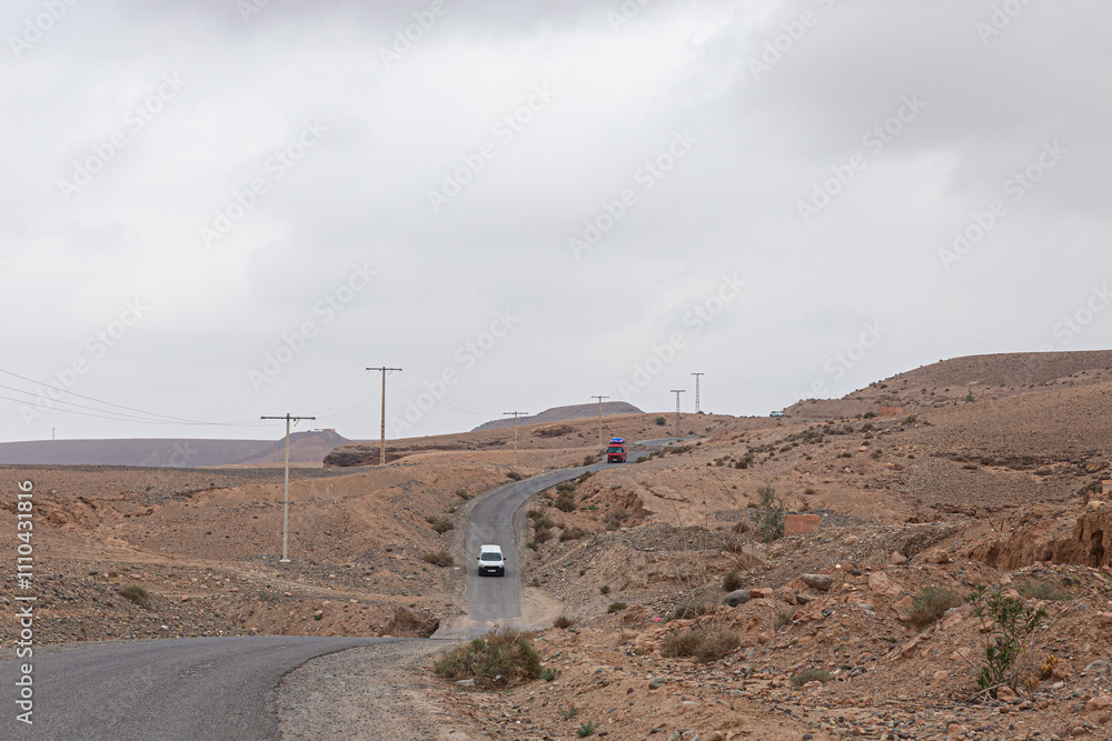 Empty Moroccan landscape with a winding asphalt road and scattered vegetation.