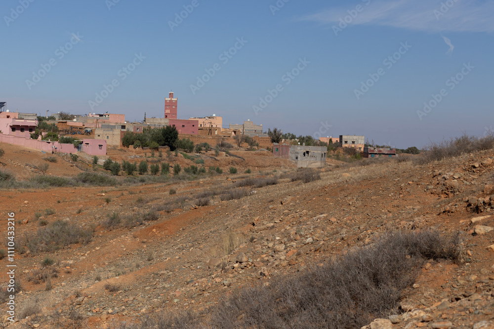 A peaceful village in southern Morocco, with a mix of mudbrick and cement houses. The Atlas Mountains rise in the distance,