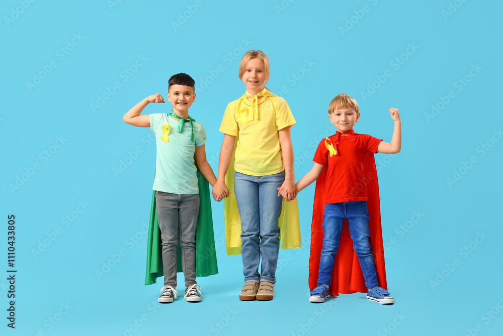 Fototapeta premium Little children dressed as superheroes with gold ribbons holding hands on blue background. Childhood cancer awareness concept